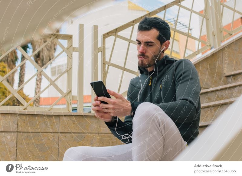 Thoughtful runner using phone taking break man browsing pensive serious training recreation stairs active male smartphone thoughtful urban street sport