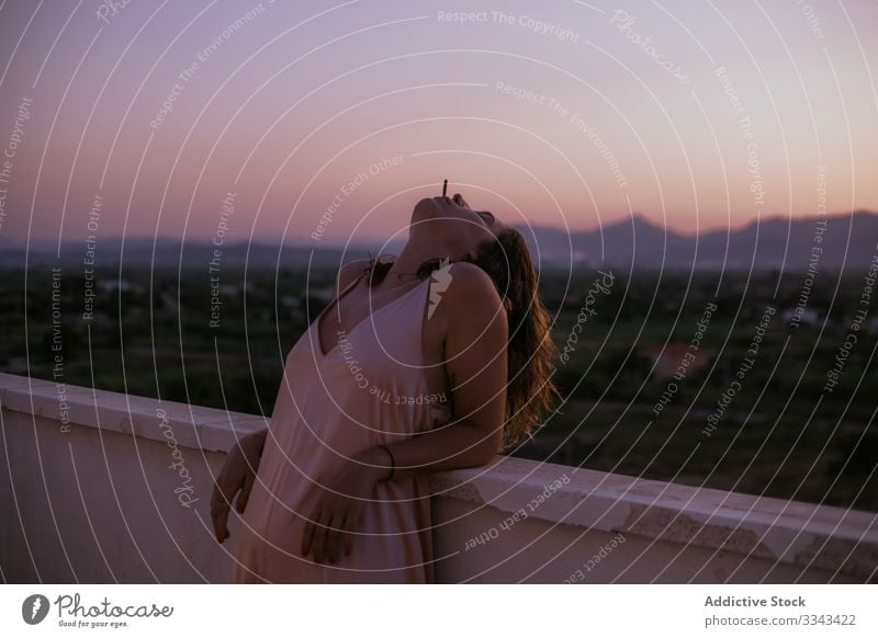 Serene woman having relaxation with cigarette on balcony smoking closed eyes lying resting fence terrace sunset evening nature sky heaven female lady lifestyle