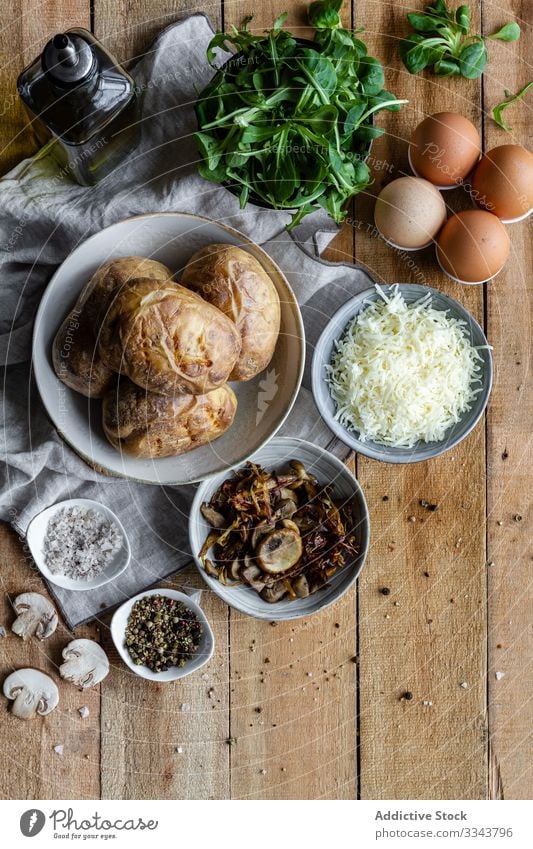 Tasty dish of potatoes and fresh ingredients on table stuffed filled rustic wooden homemade green herb spice fried mushrooms eggs grated cheese salt olive oil