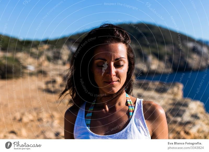 portrait of a young beautiful woman relaxed with eyes closed standing at the beach at sunset. Wind moving her hair. Vacation and relax concept