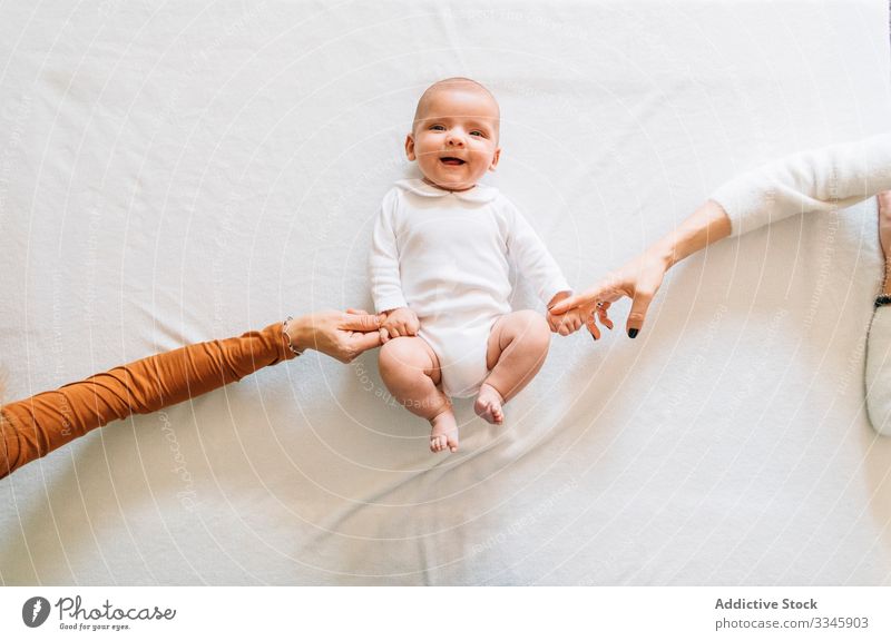 Crop women touching hands of happy baby lying bed newborn home infant bonding affection adorable child small cute kid sweet play pajama casual innocent peaceful