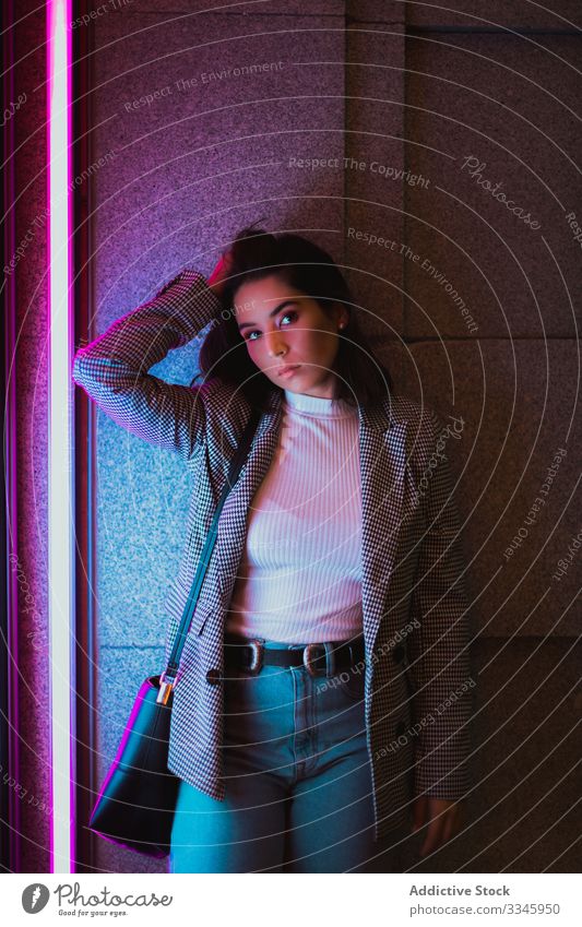 Young woman in casual outfit in neon light style clothing standing shaking head hair waving fashionable hipster millennial teenager city street urban lifestyle