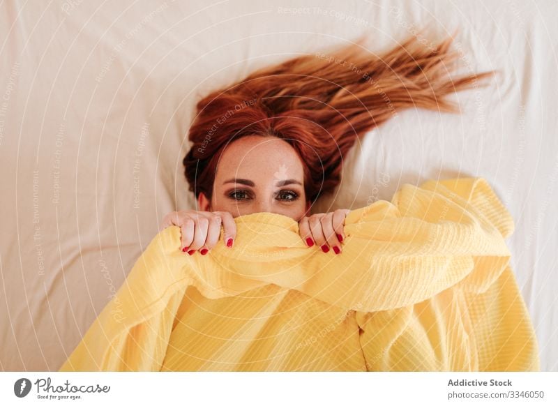 Positive lady hiding under blanket at home woman lying bed morning sitting cover yellow fun relax rest smile enjoy playful redhead lifestyle young beautiful