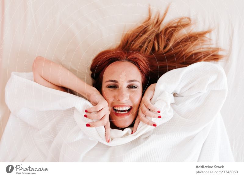 Positive lady hiding under blanket at home woman lying bed morning sitting cover fun relax rest smile enjoy playful redhead lifestyle young beautiful female