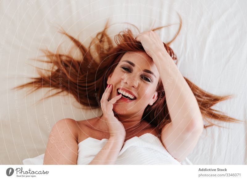 Positive lady hiding under blanket at home woman lying bed morning sitting cover yellow fun relax rest smile enjoy playful redhead lifestyle young beautiful