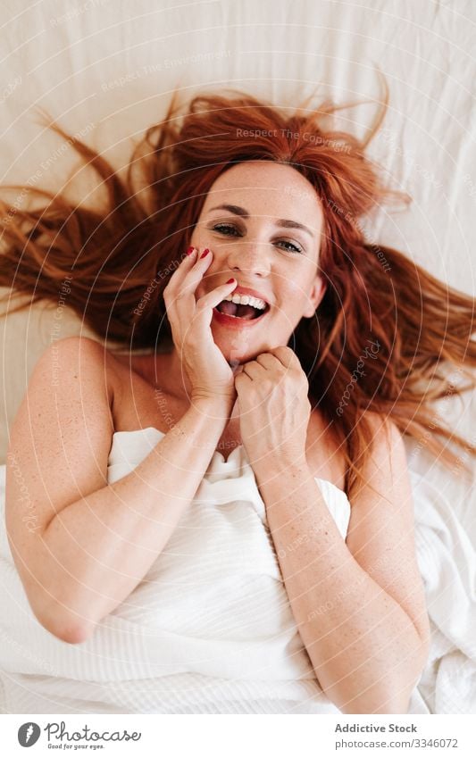 Positive lady hiding under blanket at home woman lying bed morning sitting cover yellow fun relax rest smile enjoy playful redhead lifestyle young beautiful