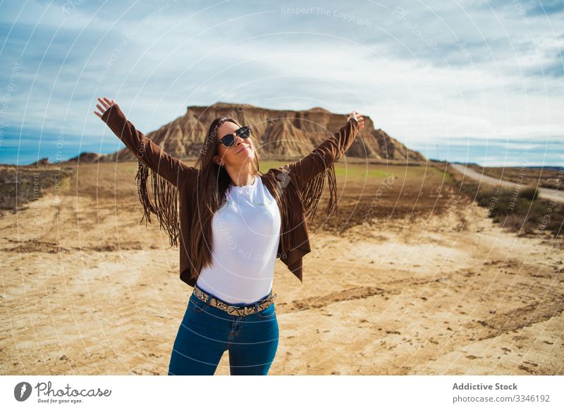 Joyful female tourist enjoying trip in desert woman travel vacation smile raised hands casual stylish sunglasses summer tourism blue sky nature lifestyle