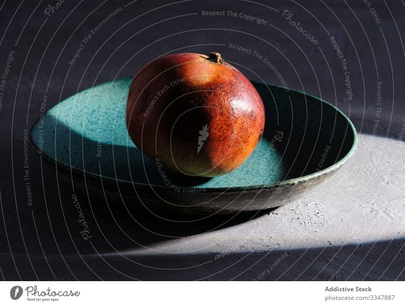 Ripe pomegranate on plate lit by ray of sunlight fruit still life organic natural single concrete exotic red fresh juicy beam health dessert agriculture diet