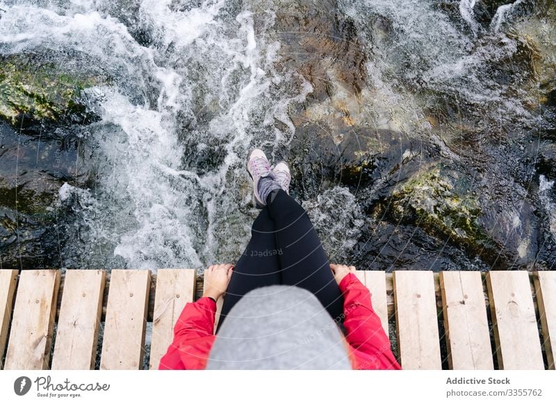 Tired tourist with backpack sitting dangling legs on bridge above mountain river village gangling legs using travel nature house peak landscape architecture