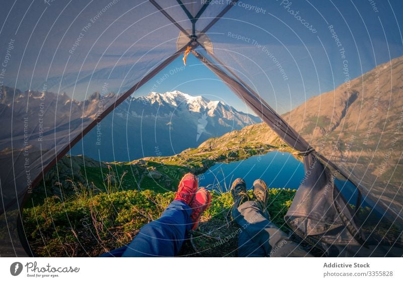 Relaxed tourists lying in tent in snowy mountains in sunlight rock lake reflection crystal clear nature travel relationship tourism camp together friendship