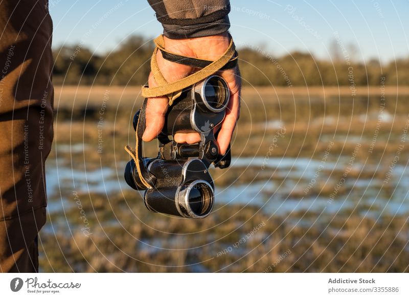 Anonymous man holding old binoculars in a lagoon water landscape forest lake wetland adventure wild fauna blue sky sunny scenic copy space nature natural