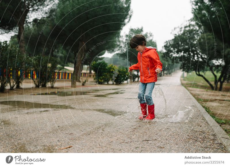 Active kid jumping in puddle in park alley child messy season funny water wet dirt childhood weather mud autumn game active rubber boots raincoat botanical