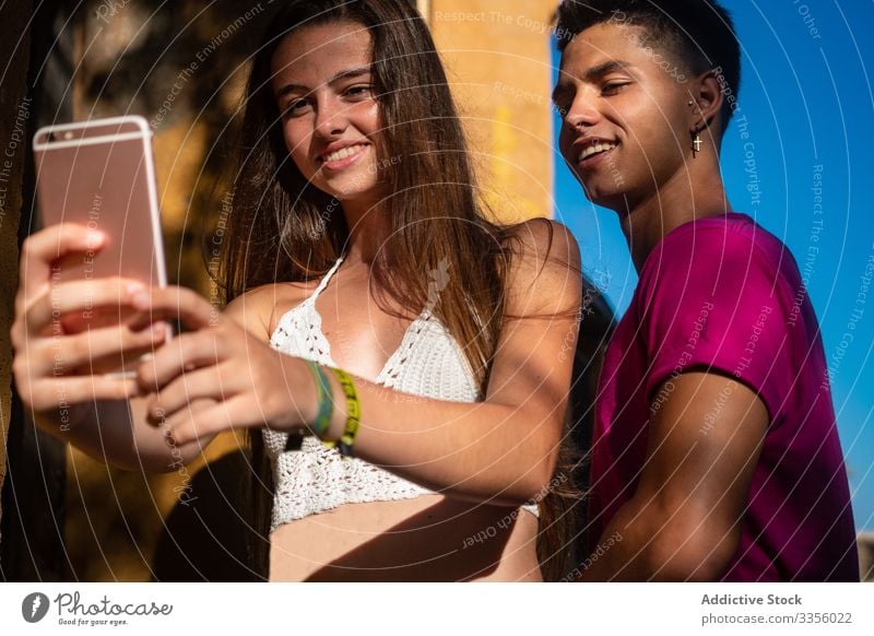 Charming young lady taking selfie on phone with content ethnic guy friend using relax smile happy handsome photograph cheerful travel vacation smartphone