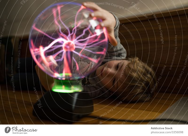 Boy looking at mysterious glass lightening lamp on table boy neon electric luminous stream ball illuminated electricity glow energy bulb bright shiny thoughtful