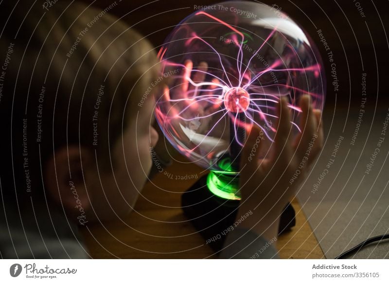 Boy looking at mysterious glass lightening lamp on table boy neon electric luminous stream ball illuminated electricity glow energy bulb bright shiny thoughtful