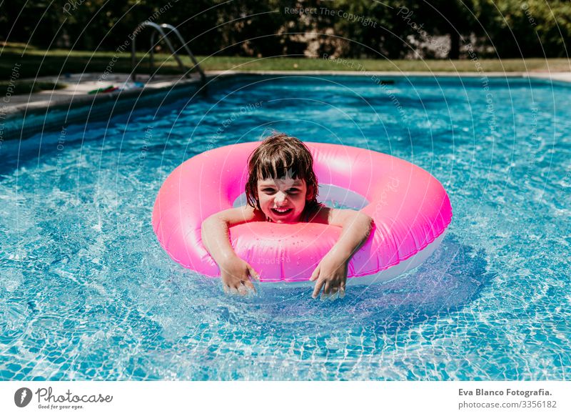 beautiful kid girl floating on pink donuts in a pool. Smiling. Fun and summer lifestyle Action Swimming pool Beauty Photography Exterior shot