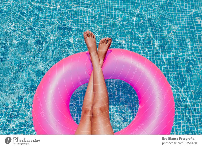 unrecognizable teenager girl floating on pink donuts in a pool. Wearing sunglasses and smiling. Fun and summer lifestyle Action Swimming pool Beauty Photography