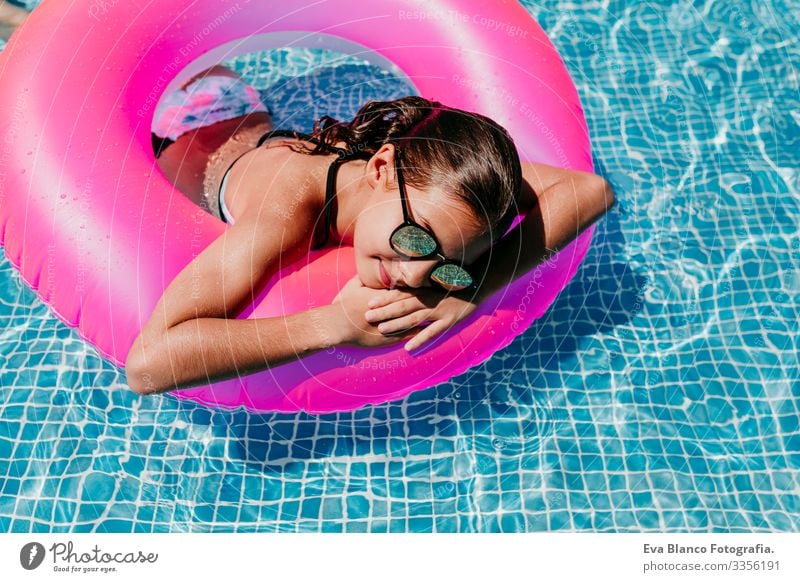 beautiful teenager girl floating on pink donuts in a pool. Wearing sunglasses and smiling. Fun and summer lifestyle Action Swimming pool Beauty Photography