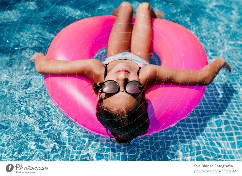 beautiful teenager girl floating on pink donuts in a pool. Wearing sunglasses and smiling. Fun and summer lifestyle Action Swimming pool Beauty Photography