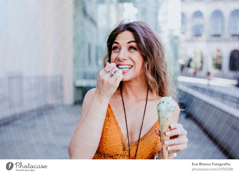 Beautiful young caucasian woman eating mint ice cream at the city street on a sunny day. Happy face smiling. Urban and summer lifestyle Day Street Woman Sunbeam