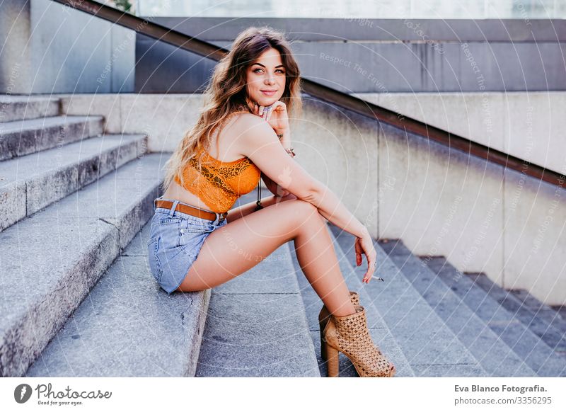 Beautiful young caucasian woman sitting on stairs at the city street on a sunny day and smoking a cigarette. Urban lifestyle and smoking concept Street Woman