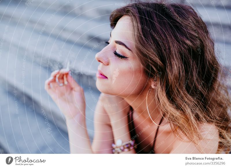 Beautiful young caucasian woman sitting on stairs at the city street on a sunny day and smoking a cigarette. Urban lifestyle and smoking concept. close up view