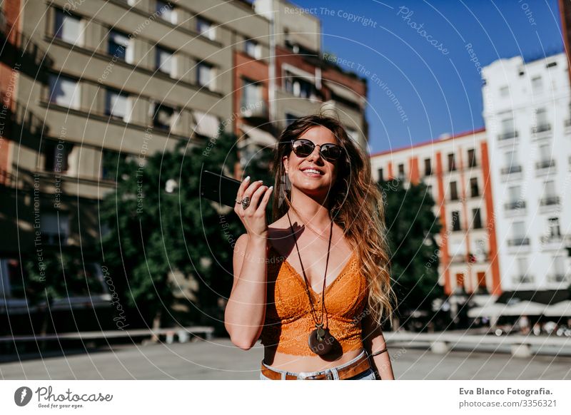 Beautiful young caucasian woman walking at the city street on a sunny day. Sending an audio with mobile phone. Happy face smiling. Urban lifestyle Day Street