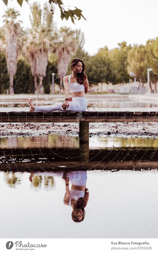 young beautiful asian woman doing yoga in a park. Sitting on the bridge with reflection on the water lake. Yoga and healthy lifestyle concept Practice