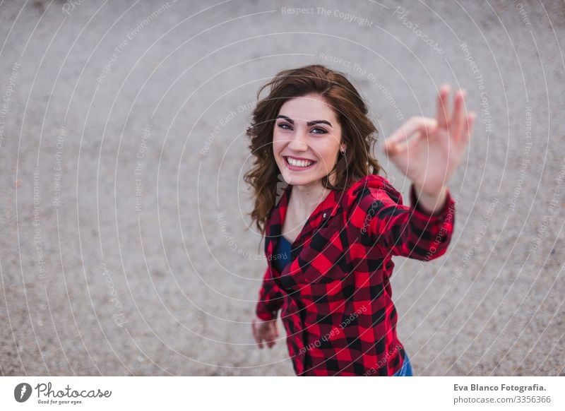 top view of a portrait of a young beautiful woman using mobile phone. She is wearing casual clothes and making ok sign with hands. Outdoors city background. Lifestyle