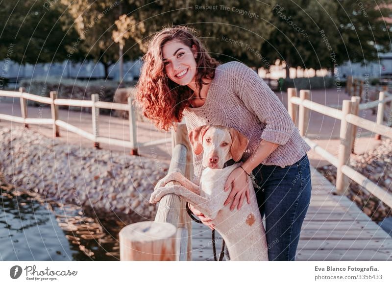 young woman and her dog outdoors walking by a wood bridge in a park with a lake. sunny day, autumn season Portrait photograph Woman Dog Park