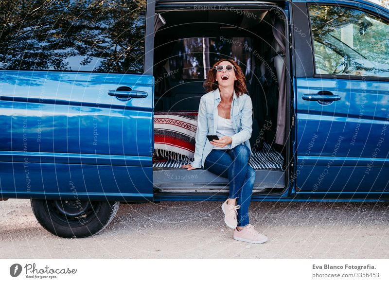 happy woman sitting in a blue van and having fun. travel concept Woman Happy Laughter Van Car Vacation & Travel Cellphone enjoying Joy Exterior shot Sit Resting