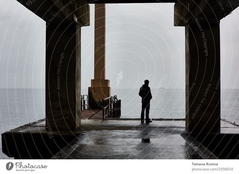 Man stands alone on a pier of sea in bad weather. Freedom Adults Fog Think Sadness Loneliness Considerate jetty Dramatic alone guy calm sea cold temperature