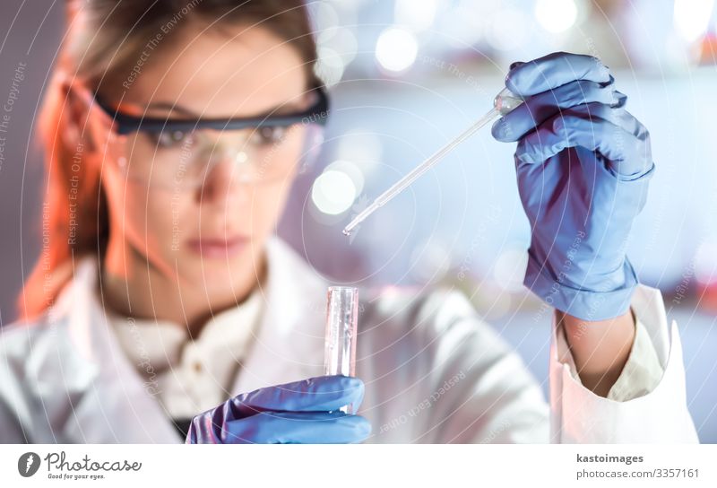 Life scientists researching in laboratory. Focused female science professional pipetting solution into glass cuvette. Lens focus on pipette. Healthcare and biotechnology. Greyscale blue toned image.