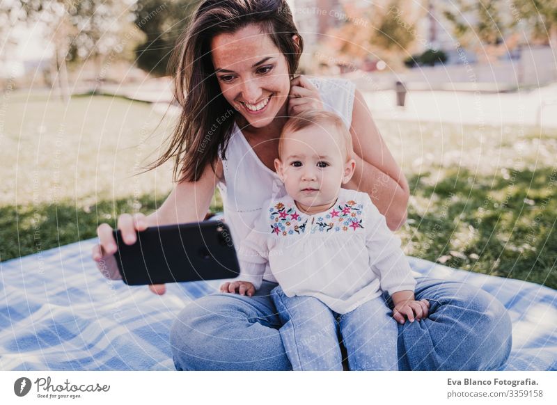 young mother and happy baby using mobile phone outdoors. technology concept Child Parenting Girl Joy Sunbeam Parents Mother Spring Baby parenthood candid