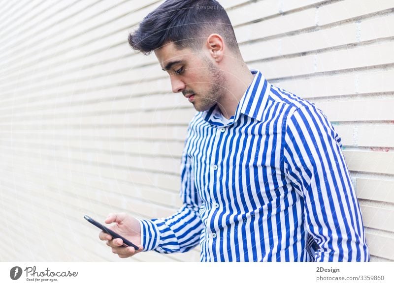 Young happy man leaning on house wall while using his smartphone Lifestyle Style Happy Business Telephone Cellphone PDA Technology Human being Masculine