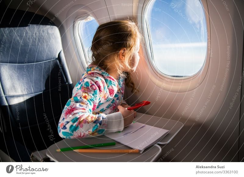 Child drawing picture with crayons in airplane. Little girl occupied while flying in aircraft. Travel with family and kids. Blue sky and sun outside the window