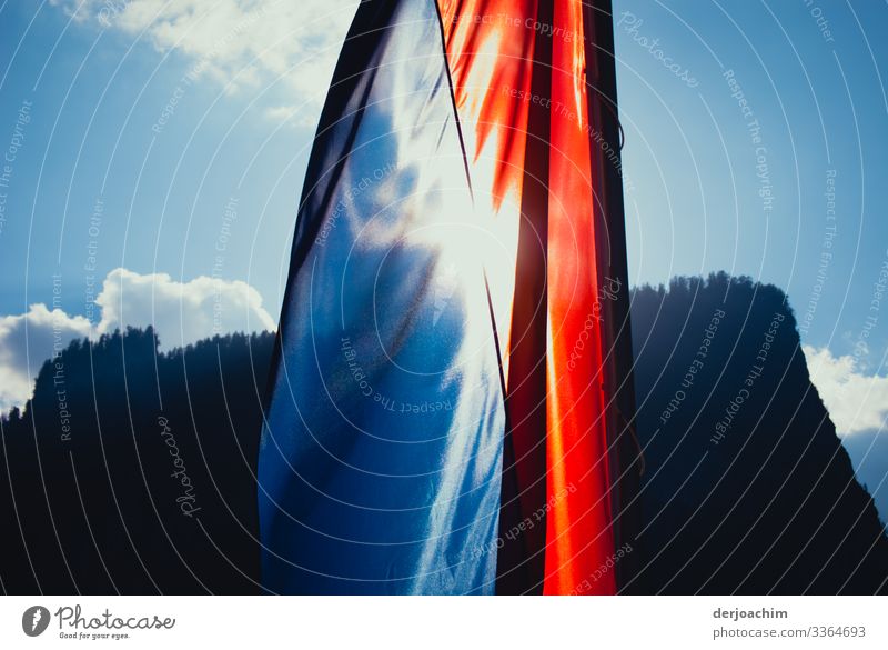 A flag is illuminated by the sun on a bridge in Salzburg. A mountain in the background. Colour photo Exterior shot Deserted Flag Day Sky Patriotism Wind