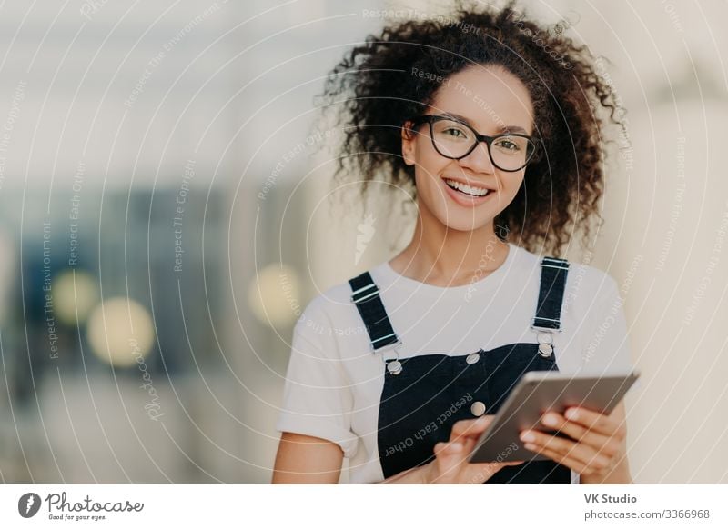 Lovely dark skinned ethnic woman holds modern touchpad Lifestyle Joy Happy Technology Internet Woman Adults Email T-shirt Shirt Eyeglasses Afro Smiling Cute