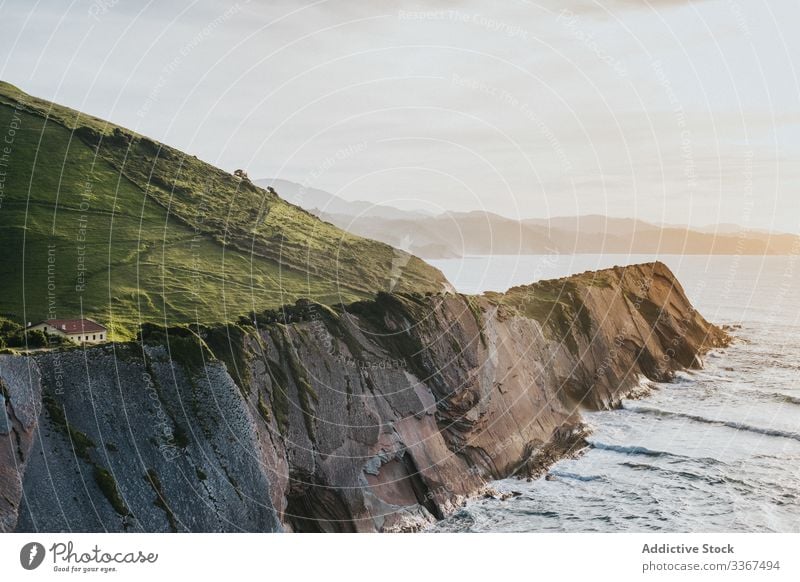 Steep rocky shore with green plain hills and houses above water coast landscape ocean sea beach bay nature travel architecture coastal scenic light building