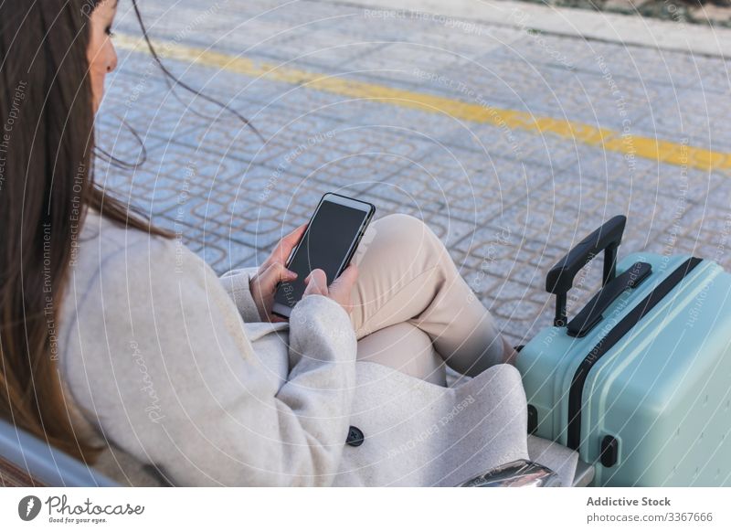 Anonymous oman waiting for train and using phone woman station mobile phone travel smartphone holiday suitcase railway bench transport terminal transportation