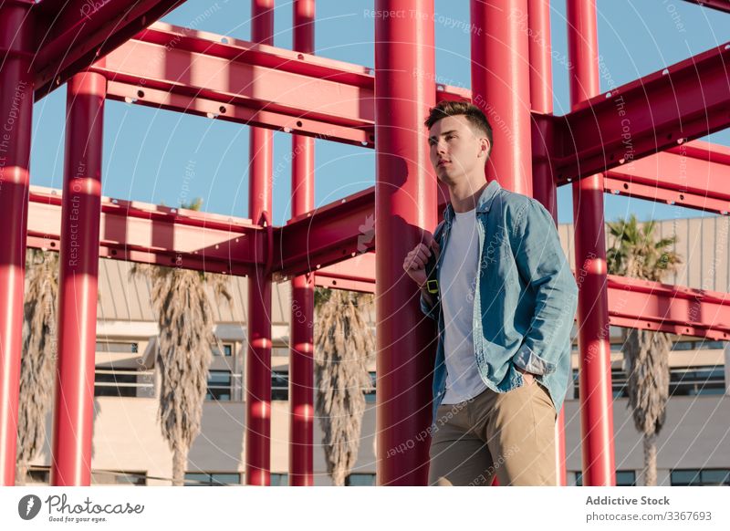 Student with backpack leaning on metal structure in bright day smart student education man campus building college youth recreation construction activity