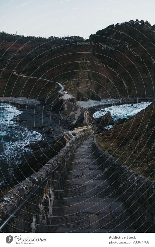 Walkway along old stone bridge and hillside under cloudless sky walkway sea shore water coast road wave fence spain trip ocean island countryside tourism