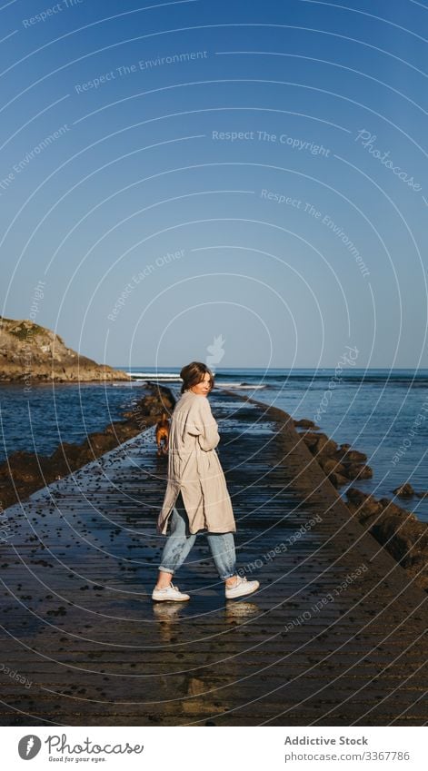 Woman with dog walking along wet pier against calm sea water and rocky coast in sunny day woman companion fresh pet ocean spain tranquil mastiff owner beach