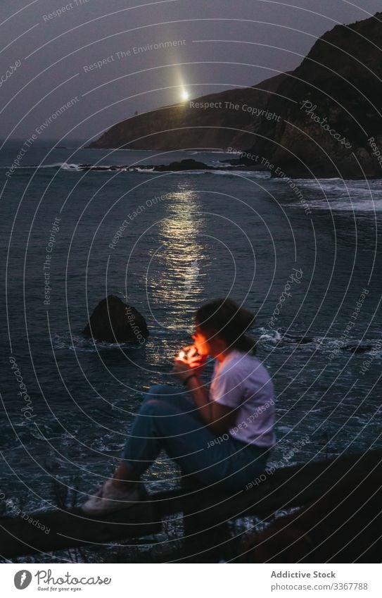 Woman smoking at seaside in evening woman coast smoke cigarette casual dusk twilight nature pensive night thoughtful relax water ocean rock stone lifestyle