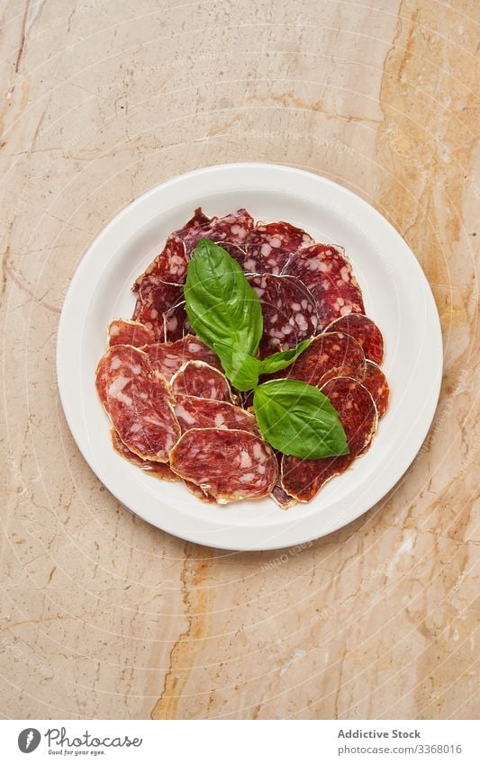 Pieces of dried meat with basil sausage slice snack smoked green leaves service decoration plate dish simple restaurant herb stylish elegant luxury salami