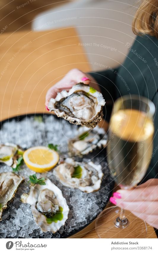 Crop person enjoying oysters and champagne eat drink restaurant lemon herb ice table clam seafood exquisite delicious tasty yummy palatable delectable savory