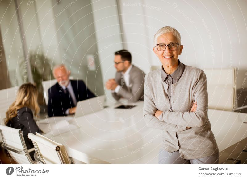 Cheerful senior businesswoman in office while other business people having meeting Lifestyle Office Business Meeting Human being Woman Adults Female senior