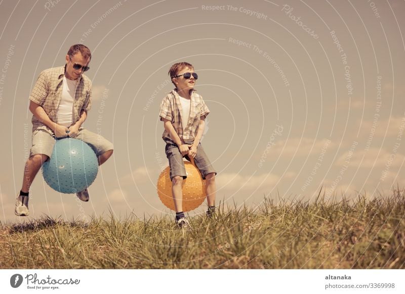 Father and son playing on the field at the day time. People having fun outdoors. They jumping on inflatable balls on the lawn. Concept of friendly family.