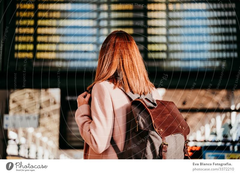 young woman at train station looking at destination board. Travel and public transport concept screen travel backpack back view caucasian europe railway waiting