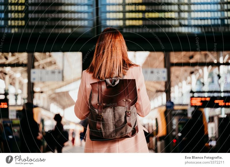 young woman at train station looking at destination board. Travel and public transport concept screen travel backpack back view caucasian europe railway waiting